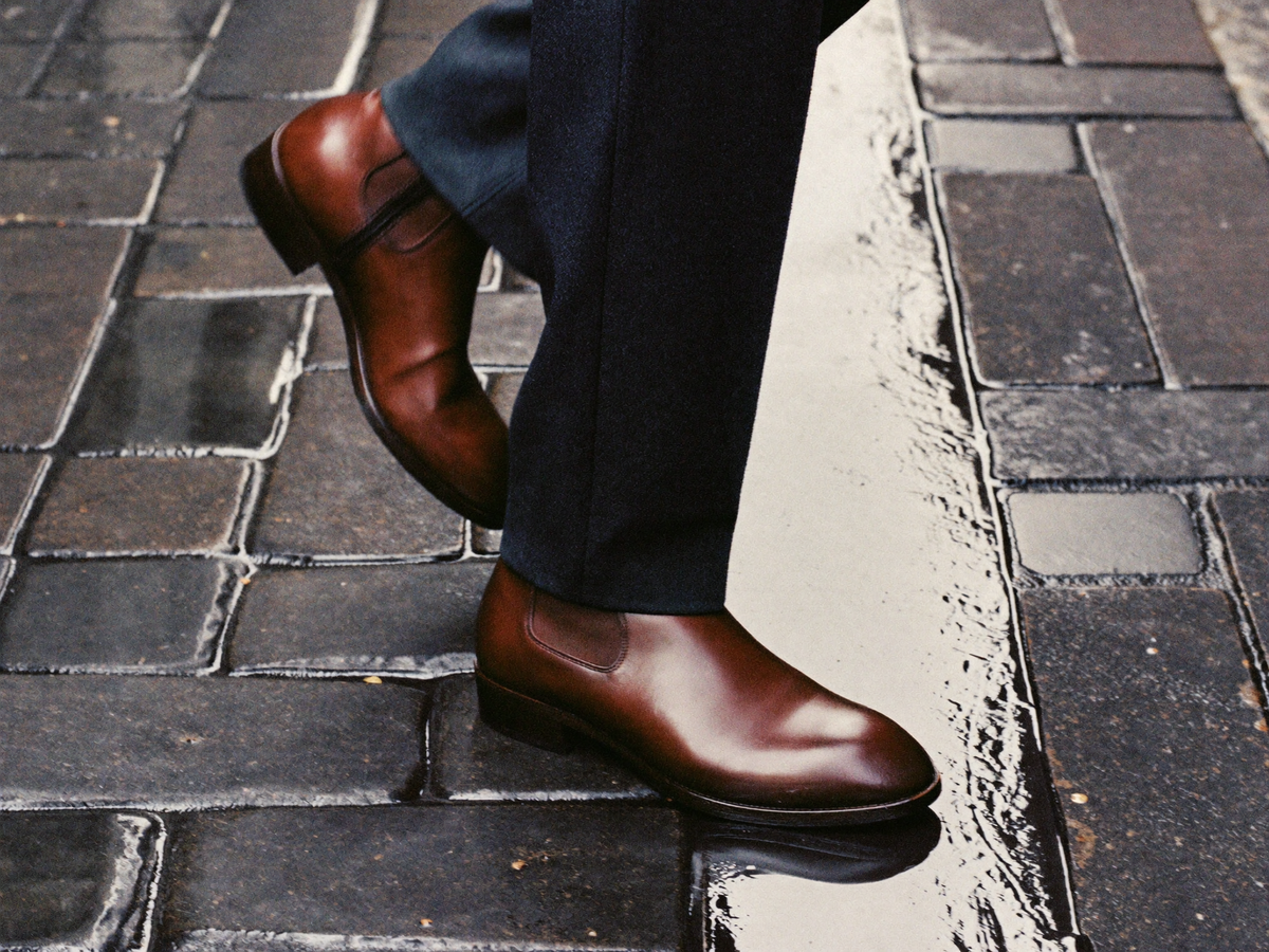 Brown leather slip-on dress shoes on wet cobblestones