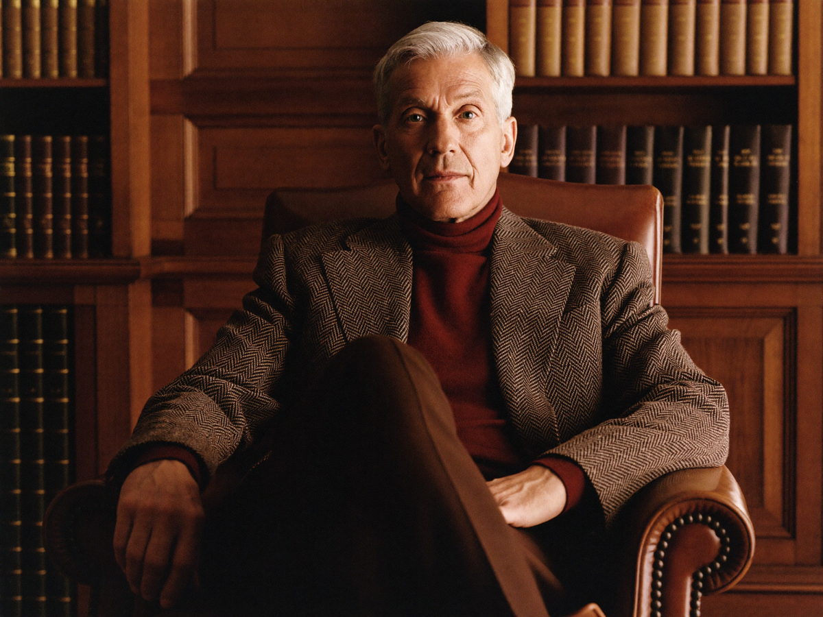 Man in a brown herringbone tweed blazer and roll neck in a panelled study