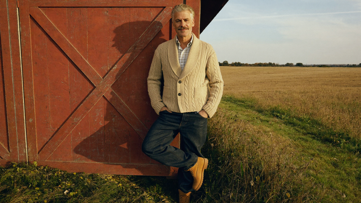Man in an oatmeal shawl-collar cable cardigan beside a red barn door