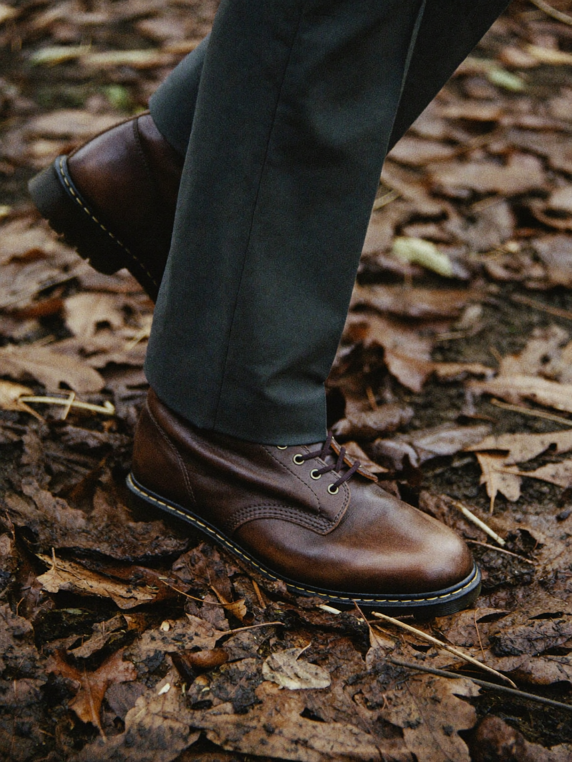 Brown leather lace-up boots on wet autumn leaves