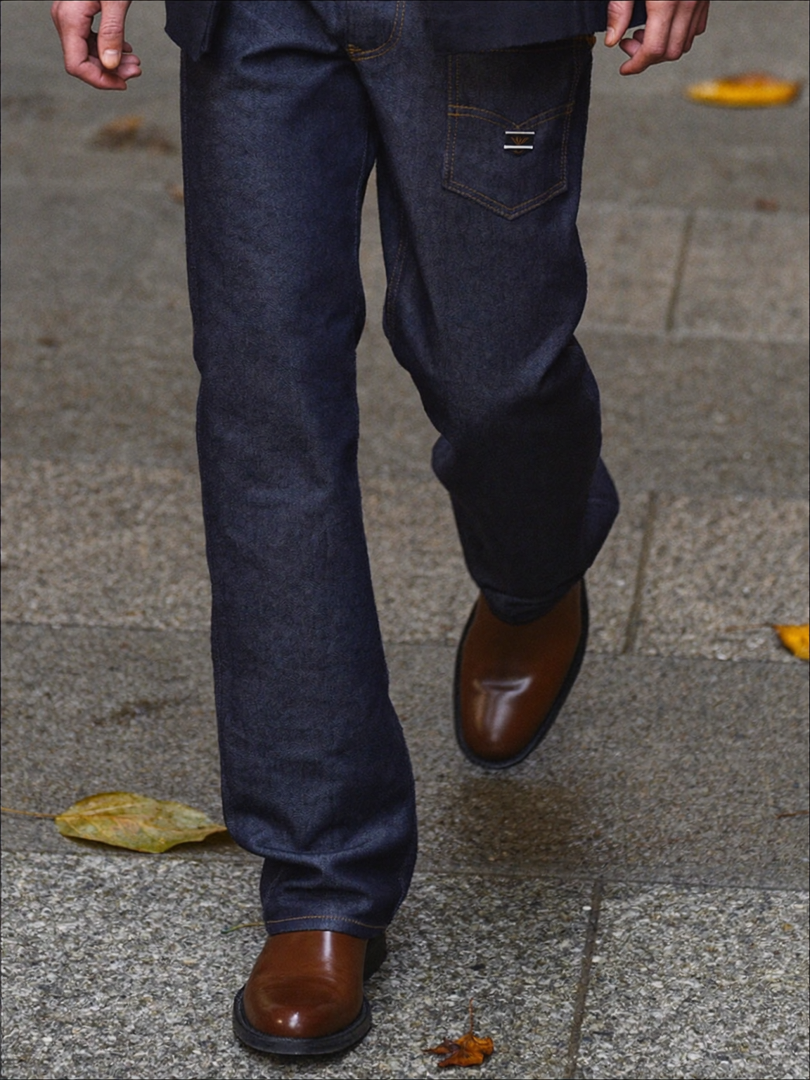 Dark indigo jeans and brown leather boots walking on a wet autumn pavement