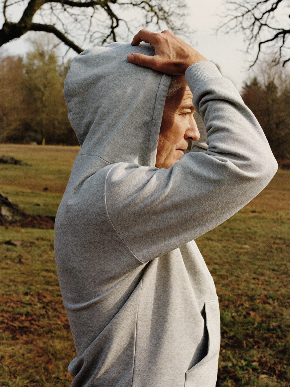 Man in a grey hooded sweatshirt pulling the hood up outdoors
