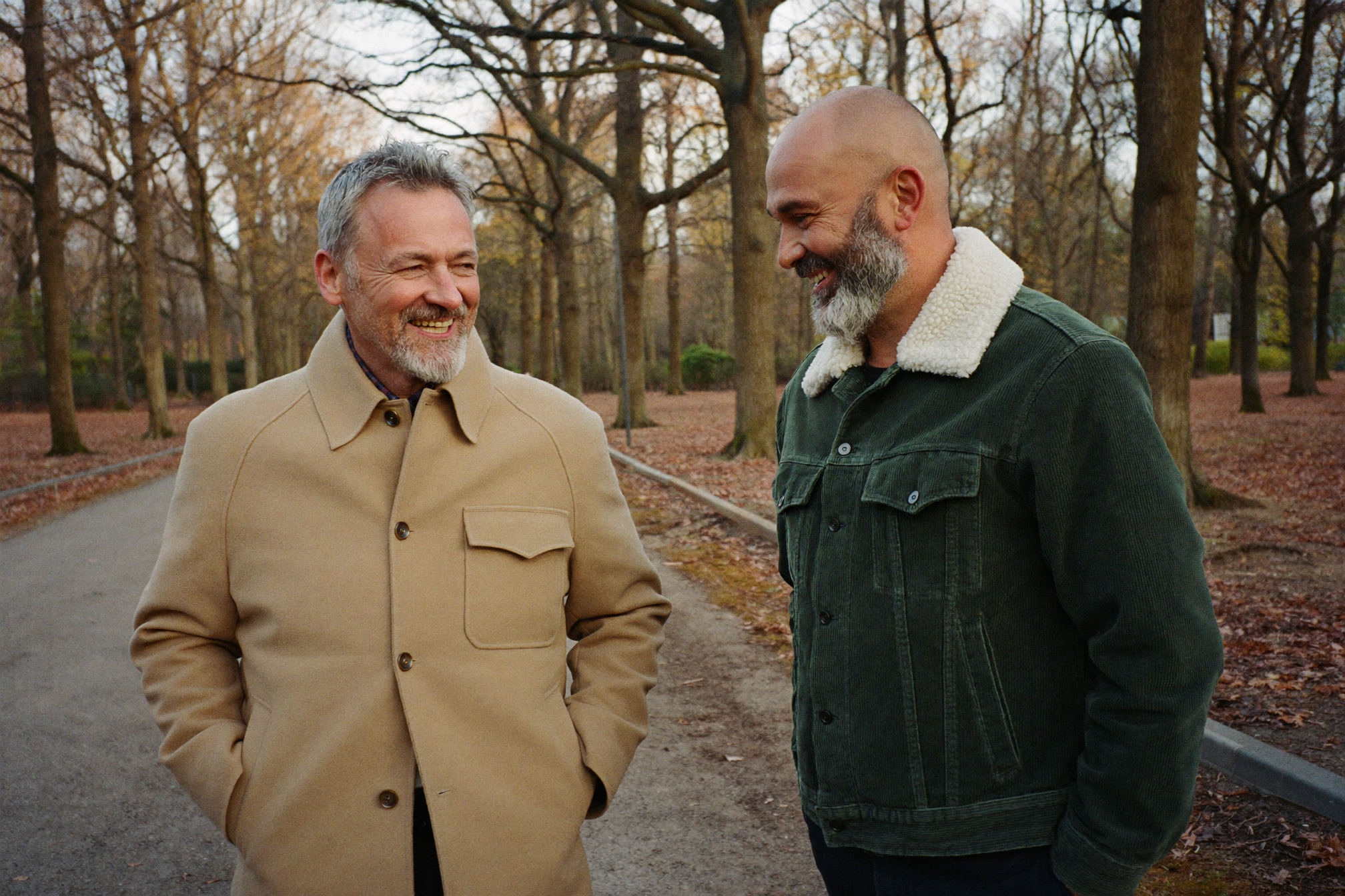 Two men in autumn coats talking on a park path